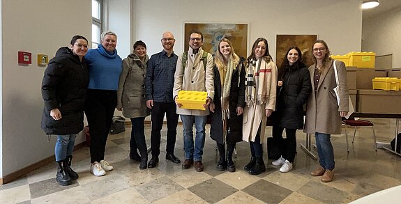 Gruppenfoto von neun LEGO® SERIOUS PLAY Trainer*innen nach einem Großgruppenworkshop. Das TEAMWILLE-Trainingsteam steht gemeinsam vor einer Präsentationsfläche und lächelt in die Kamera.