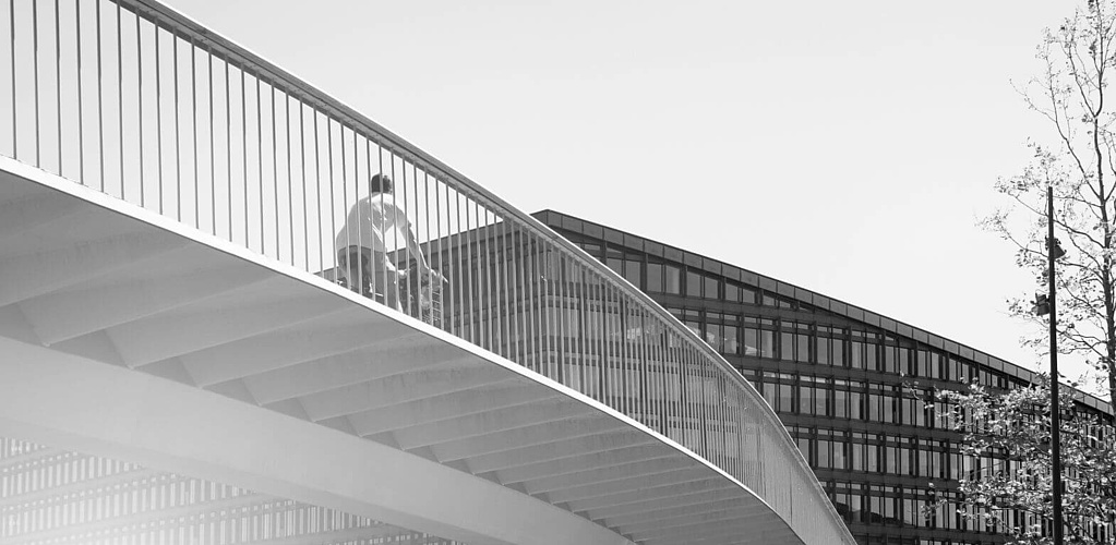 Radfahrer fährt über eine Brücke auf ein Bürogebäude zu